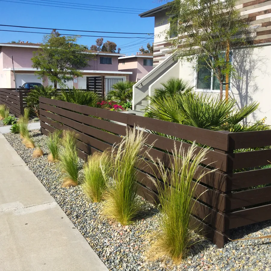 Modern home with a horizontal wood-slat fence, ornamental grasses, and gravel planting along the walkway